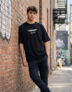 Person wearing a black t-shirt with text, leaning against a brick wall in an urban setting.